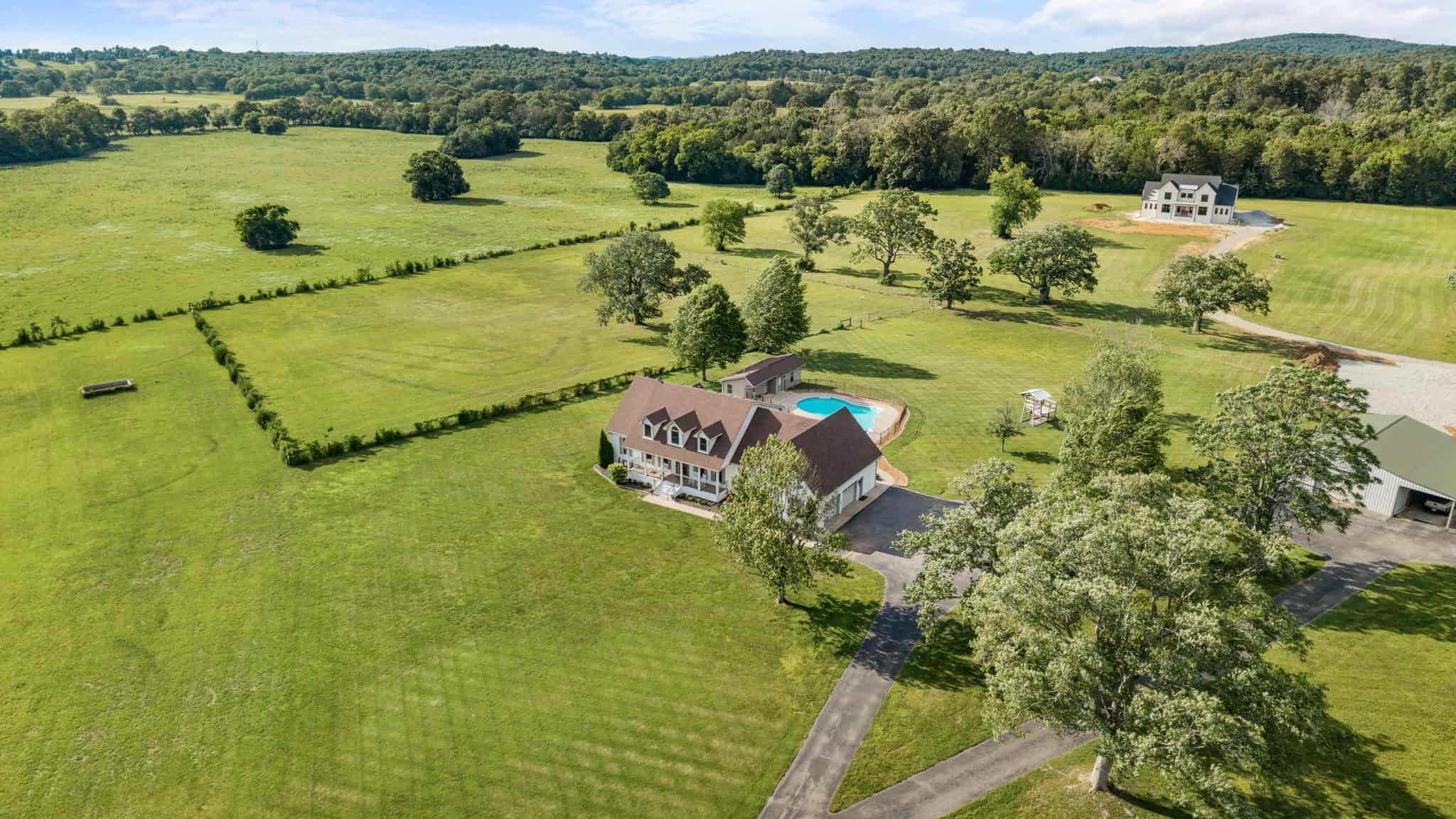 Spacious countryside estate with a large house, pool, and expansive green fields.