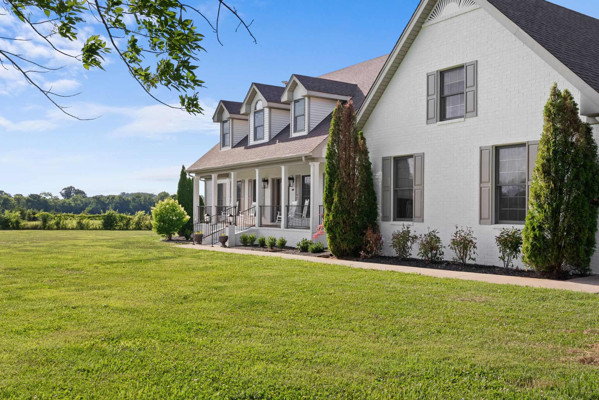 Spacious white house with a large front yard and lush greenery.