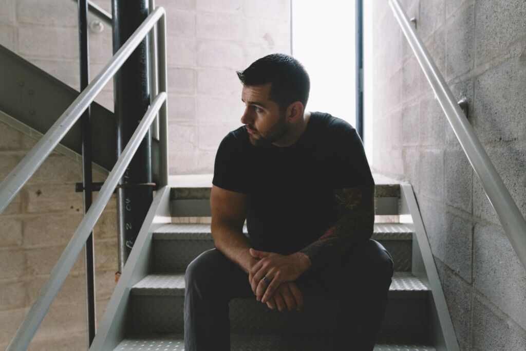 Young man sitting on stairs, looking distressed, with backpack nearby.