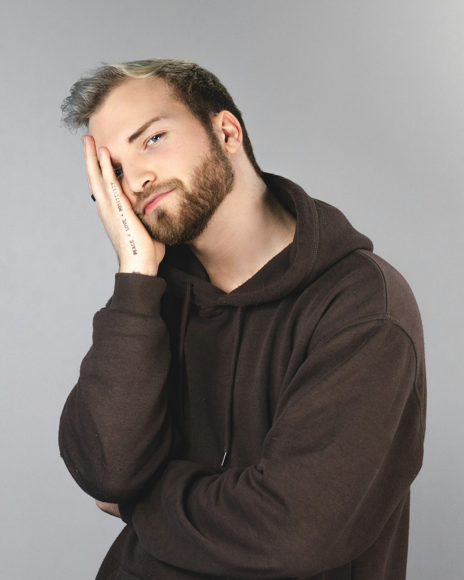 Person in blue hoodie covering face with hand, emotional distress.